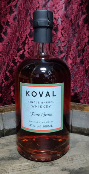 一瓶Koval Four Grain威士忌放在木頭上，背景是紅色蕾絲。