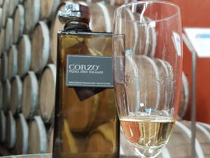 一瓶Corzo龍舌蘭酒放在一杯金色液體旁邊，前面是木桶。