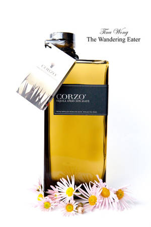 一個Corzo Tequila Añejo酒瓶被粉紅色雛菊環繞，背景為白色。