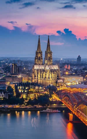 科隆大教堂在黃昏時閃耀，河流和橋燈倒映在水中。 — Galaxy Tab 壁紙