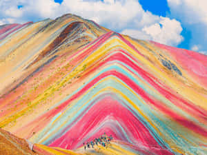 徒步旅行者在陽光明媚的藍天白雲下攀登彩虹色的山。 — 紅色山脈 壁紙