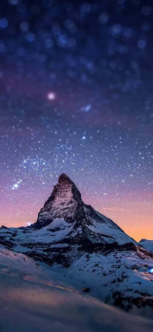 積雪的山峰在紫色和橙色色調的星空暮色天空下。 — iPhone 14 Plus 壁紙