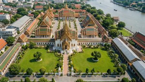 河邊擁有金色屋頂和綠色草坪的宏偉泰國寺廟建築群的鳥瞰圖。