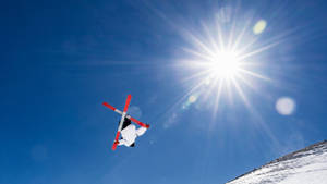 滑雪運動員在半空中，以明亮的太陽和白雪覆蓋的山坡為背景表演技巧。 — 冬天 壁紙