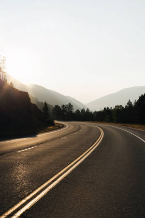 日出時穿過山脈的彎曲道路，兩旁是森林。