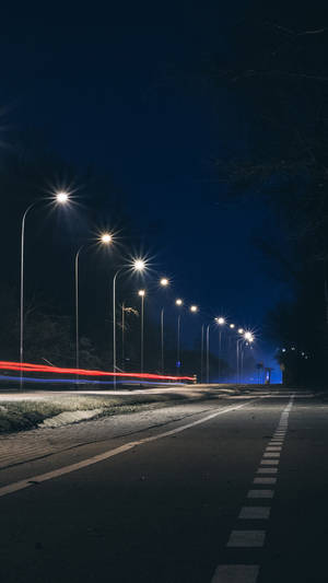 夜晚街道，有發光的燈和來往車輛留下的紅色光跡。