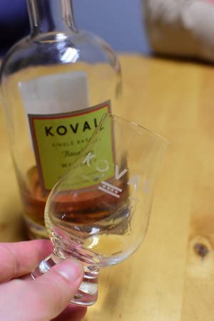 手揸住Koval威士忌品酒杯，背景有酒樽。