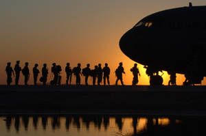 剪影士兵在日落時分在水面倒影旁排列在軍用飛機旁邊。