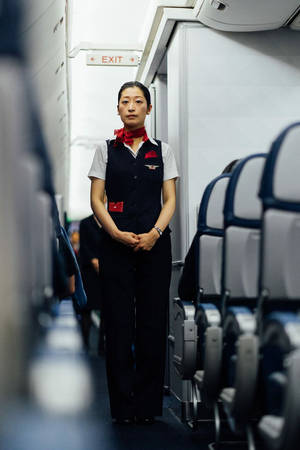 一位空中服務員站在飛機走廊中，座位排之間。