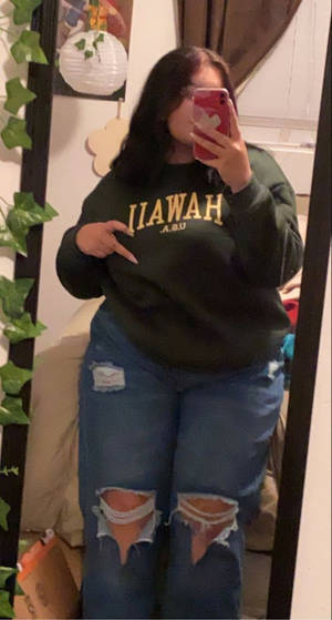 穿著綠色衛衣和破洞牛仔褲的人在裝飾過的房間裡對著鏡子自拍。