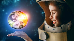 穿著紙板太空衣的小孩抱著發光的地球在太空中。