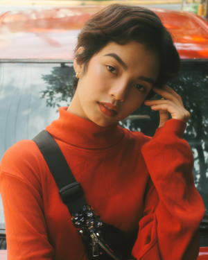 年輕女子身穿紅色高領毛衣在日落時分站在紅色汽車旁