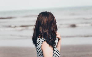 身穿波點裙的女子站在沙灘上面向海洋