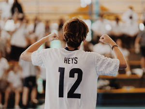 年輕運動員身穿白色球衣印有HEYS 12，在體育館內面對歡呼的人群彎曲手臂。