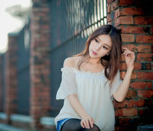 年輕女性身穿白色上衣靠喺戶外磚牆上