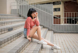 年輕女性戴著太陽眼鏡和珊瑚色毛衣坐在戶外瓷磚台階上。 — 模特兒 GIF 壁紙