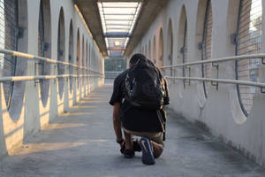一個人跪喺混凝土橋嘅行人路上，有拱形窗戶同欄杆。