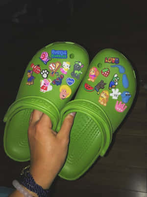綠色Crocs鋪滿卡通貼紙，由手拎住喺木地板上。
