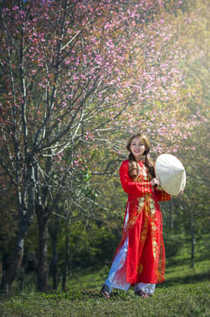 身穿紅色傳統服飾和圓錐形帽子的女性在櫻花樹下微笑。