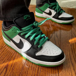 木地板上黑色、白色和綠色Nike SB Dunk Low Pro運動鞋。