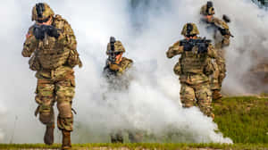 穿著迷彩裝備的士兵在草地上穿過煙霧移動。 — Pro Display XDR 壁紙