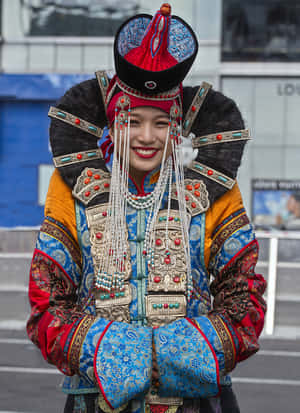 一位身穿鮮豔傳統服飾的女士在城市環境中溫暖微笑。 — 亞洲 壁紙