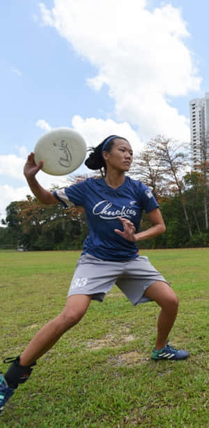穿藍色球衣的女飛盤選手在高樓附近的草地上擲盤。 — 飛碟 壁紙