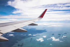 飛機機翼飛越熱帶島嶼和海洋，伴隨著白雲