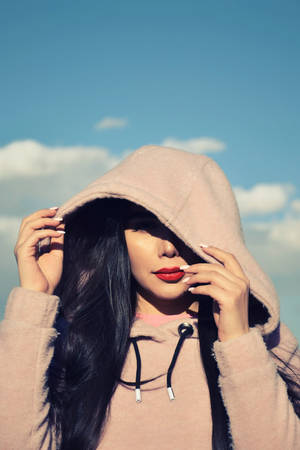 身穿粉紅色連帽衫的女性在藍天下調整帽子