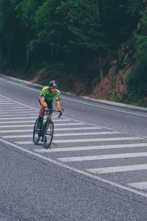 身穿綠色運動衫的單車手在森林環繞的山路上穿過斑馬線。