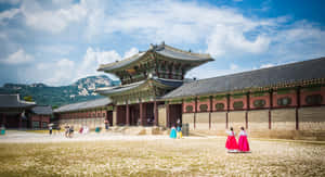 穿著傳統韓服的人們在歷史宮殿附近行走，背景是山脈。