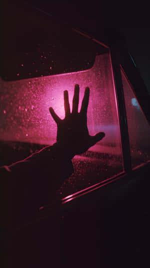 一隻手按喺落雨嘅窗上，被粉紅色光照亮。