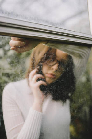 身穿白色毛衣的女性在雨痕斑斑的窗戶後打電話 — 美學手機GIF 壁紙