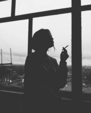 女人剪影在窗邊抽煙，俯瞰城市