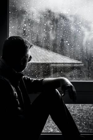 剪影男人坐在雨窗邊看著雪景
