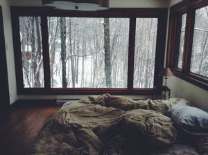臥室中未整理的床，透過大窗戶可看到雪森林景色。 — 冬天 壁紙