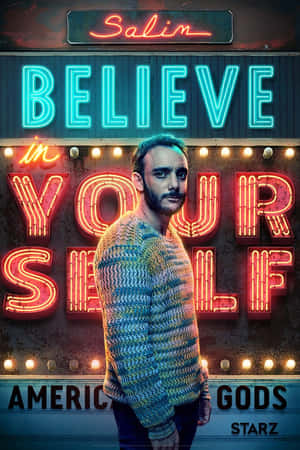 身穿針織毛衣的男子站在發光的「Believe in Yourself」霓虹燈牌前，為American Gods宣傳。 — 聖經天使 壁紙