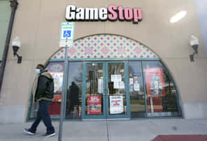 一個戴著口罩的人走過一間有玻璃門和折扣標誌的GameStop商店。 — 遊戲 壁紙