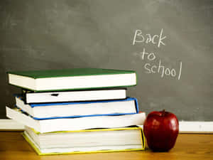 桌上的一堆學校課本和紅蘋果，黑板寫著Back to School