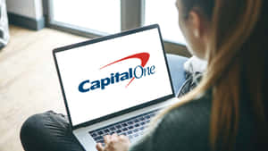在室內窗邊使用顯示Capital One標誌的筆記型電腦的人