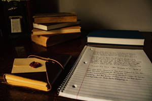 一本帶有手寫筆記的筆記本放在皮革日記本和一堆書旁邊的木桌上。
