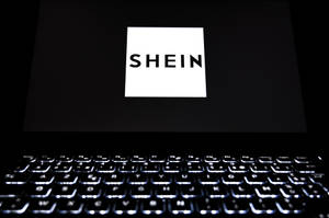 手提電腦屏幕顯示SHEIN標誌，鍵盤在黑暗房間中發光