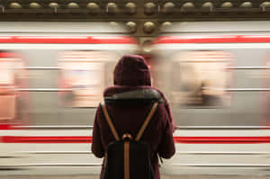 穿著栗色外套的人在夜晚的車站等待地鐵列車模糊地駛過。