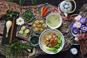 亞洲美食，包括麵條、餃子、湯和裝飾，擺放在圖案布上。