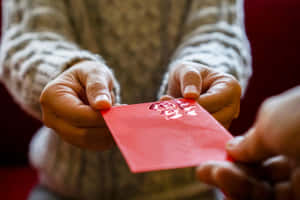 兩隻手交換帶有金色中文字的紅色利是封。 — 紅色美學 壁紙
