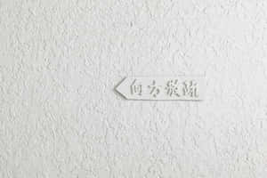 帶有日文文字的白色方向標誌，位於有紋理的牆上。