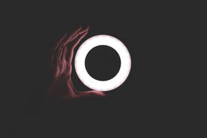 手拿著一個發光的白色戒指，背景為深色。 — 簡約 壁紙