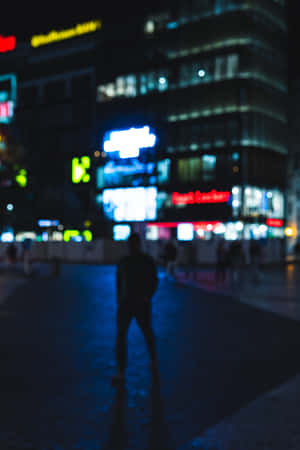 夜晚濕漉漉的城市街道上，發光霓虹燈招牌下的模糊人影。