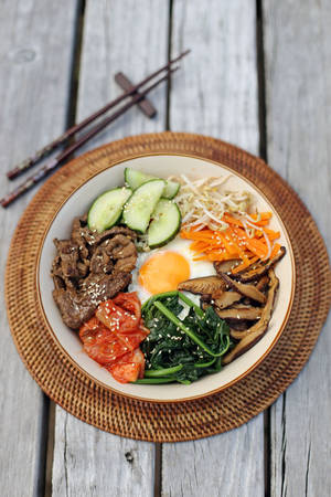 色彩繽紛的韓國石鍋拌飯，配有牛肉、雞蛋和蔬菜，放在木桌上，附有筷子。 — 清新 GIF 壁紙