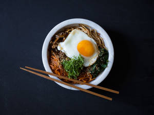 一碗韓國米飯料理，上面放著太陽蛋和蔬菜，附有筷子。 — 極簡美學 壁紙